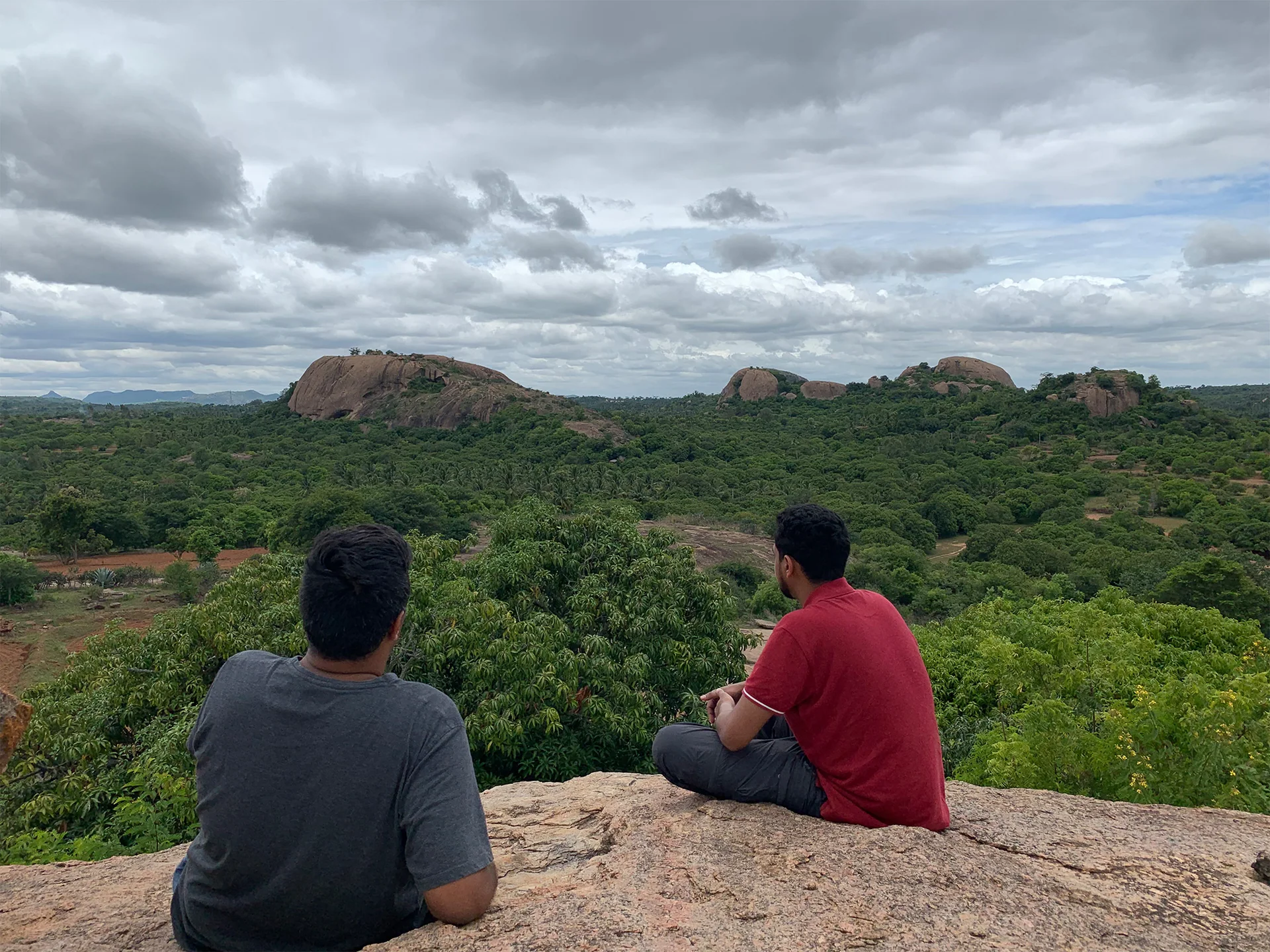 Two visitors sitting on a rocky hill overlooking the green landscape.